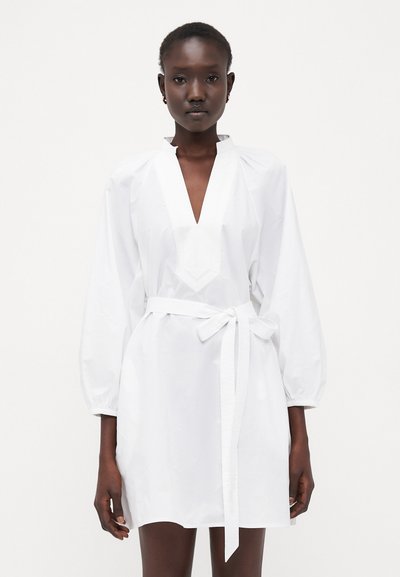 Witte jurk met een v-hals en gathered mouwen, voorzien van een strikriem in de taille. Glad textuur en minimale ontwerpelementen.