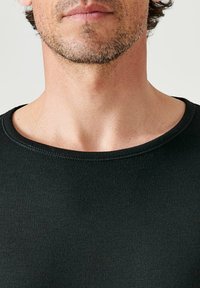 T-shirt noir ajusté avec un col rond, fabriqué à partir d'un tissu extensible et lisse. Présente des coutures visibles le long de l'encolure.