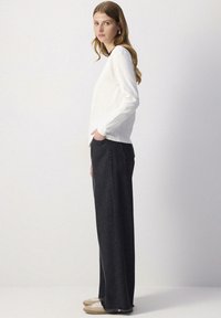 Tricou alb cu mâneci lungi, blugi negri cu talie înaltă și croi larg, cu margini destramate, asortați cu adidași ușori. Design simplu, croi lejer.