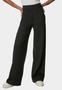 Pantaloni neri a gamba larga realizzati in un tessuto morbido, con vita alta e una texture liscia. Abbinati a sneakers bianche per un contrasto.