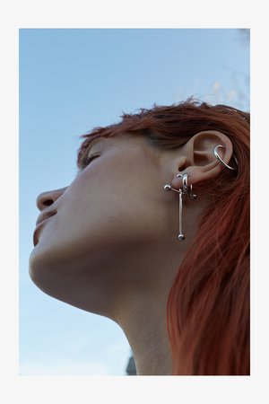 Silberohrringe mit geometrischen Formen, die Stäbe und Kugeln enthalten. Das Design umfasst mehrere Ringe und ein längliches Hauptstück.