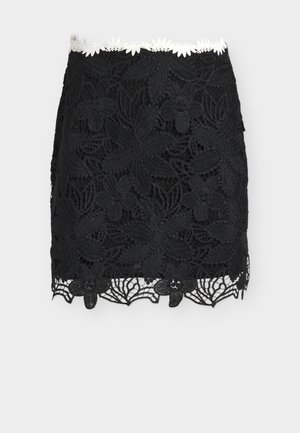 Mini-jupe en dentelle noire à motifs floraux avec un bord en marguerites blanches à la taille, présentant des détails découpés complexes le long de l'ourlet.