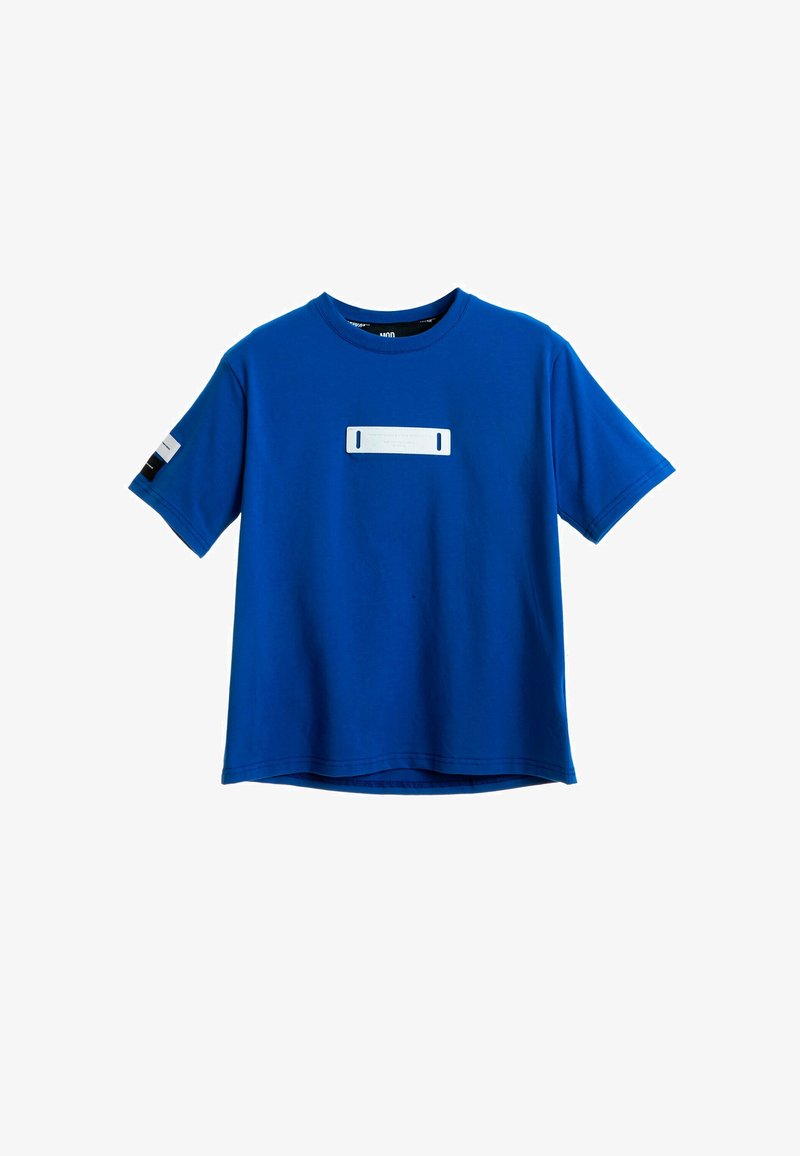 Camiseta de algodón azul con mangas cortas, escote redondo, con un panel rectangular blanco en el frente y un detalle negro en la manga.