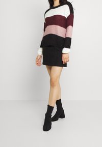 Pletený svetr s červenými, růžovými, černými a bílými vodorovnými pruhy; doplněný černou semišovou minisukní a černými kotníkovými botami.