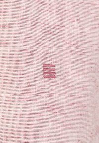 Gestructureerde stof met een roze tint, met een klein geborduurd logo van drie horizontale lijnen in een contrasterende kleur.