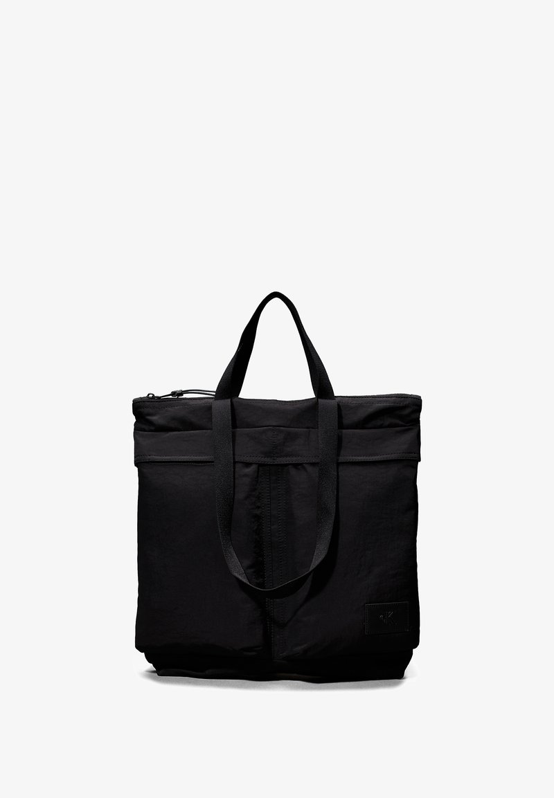 Sac fourre-tout noir en tissu avec deux poignées supérieures, fermeture éclair, surface texturée et un logo en relief subtil à l'avant.