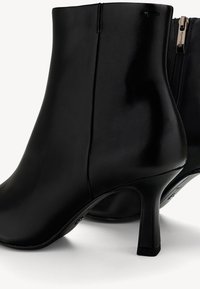 Bottines en cuir noir avec talons hauts et fins et fermeture éclair sur le côté, présentées sur un fond clair.