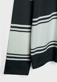 Crna i svijetlozelena tkanina sa prugama, sadrži horizontalne linije i mekanu teksturu. Manšete i rub su uredno ušiveni.