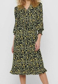 Vestido negro con estampado floral amarillo, escote en forma de V y mangas abullonadas. Presenta una cintura ceñida y un dobladillo con volantes. Textura de tejido suave.