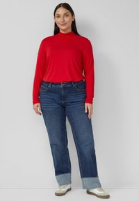 Czerwona bluzka z długim rękawem w połączeniu z niebieskimi dżinsami z podwiniętym brzegiem oraz beżowymi trampkami z jasnymi akcentami. Prosty fason, jednolite kolory i casualowy krój.
