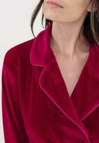 Ropa de terciopelo carmesí con un cuello muescado y piping en contraste, textura suave y un corte holgado, que muestra un caído suave.