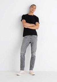 Mustat lyhyet hihaiset T-paidat, harmaat kuluneet farkut, joissa on polvielle ja taskuille yksityiskohtia, sekä valkoiset tennarit. Slim fit, kevyttä kangasta.