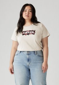 Beige bomull t-skjorte med et blomstrete Levi's logo-design, sammen med lyseblå høy midje denimjeans. Enkel rund hals og avslappet passform.