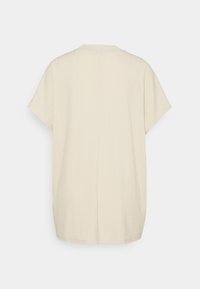 Ljusbeige kortärmad topp med rund halsringning, med texturerat tyg och en diskret mittsöm på ryggen.