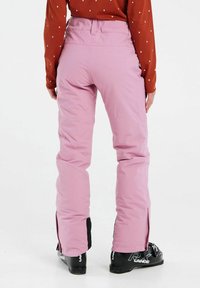 Ružové zateplené lyžiarske nohavice so zúženým strihom, viditeľné zipsy na členkoch a hladkou textúrou, v kombinácii s čiernymi lyžiarskymi topánkami.