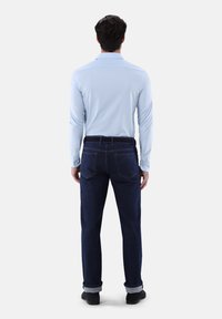 Hellblaues Langarmhemd mit Kragen, kombiniert mit dunklen Jeans aus Denim. Die Jeans haben ein klassisches Fünf-Taschen-Design und umgeschlagene Säume.