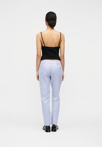 Μαύρο τοπ με λεπτές τιράντες, ανοιχτόχρωμο λιλά παντελόνι με πίσω τσέπη και μαύρα παπούτσια· απεικονίζεται από πίσω με φόντο ένα απλό φόντο.