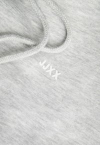 Sivi dukserica od teksturiranog materijala, sa pletenom ušiljkama i bijelim izvezenim logotipom "JUXX" na prednjoj strani.