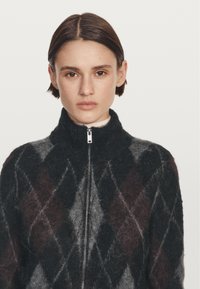Czarny i szary sweter na suwak z diamentowym wzorem w odcieniach bordo, z wysokim kołnierzem i miękkim, teksturowanym wykończeniem.