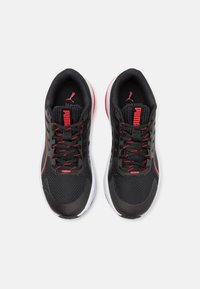 Baskets de course en mesh noires avec des accents rouges, présentant une tige texturée, des lacets solides et une semelle en caoutchouc blanche. Logo PUMA visible sur la languette.
