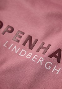 Rosa tyg med stort tryckt text "KOPENHAMN" i mörkbrunt och "LINDBERGH" i vitt, med en slät textur.
