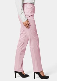 Lichtroze broek met een gladde textuur, elastische tailleband en zijzakken, gecombineerd met zwarte hoge hakken, weergegeven vanuit de zijkant.