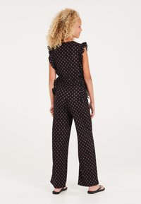 Jumpsuit nero a fantasia con maniche corte a volant, pantaloni larghi e un motivo floreale in rosa. Tessuto leggero, stile casual.