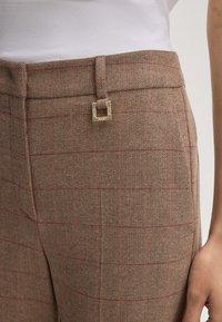 Bruine houndstooth broek met een subtiel roze ruitpatroon, voorzien van een vierkante gouden taille-clasp en een zachte, op maat gemaakte afwerking.