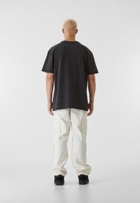 Čierne bavlnené tričko s krátkymi rukávmi, kombinované s krémovými cargo nohavicami. Oblečenie má voľný strih a čiernu obuv.