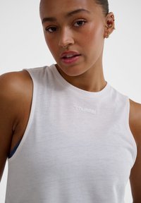 White sleeveless athletic top made of breathable fabric, featuring a subtle texture and a logo in the center of the chest area.