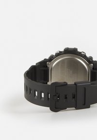 Montre de sport en caoutchouc noir avec un bracelet texturé, un dos en métal et une boucle réglable. Présente plusieurs boutons et des détails découpés.