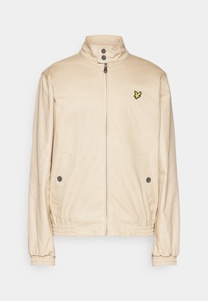 Beige, leichte Jacke mit hohem Kragen, Reißverschluss, zwei Seitentaschen und elastischen Bündchen. Auf der Brust befindet sich ein kleines gelbes Logo.