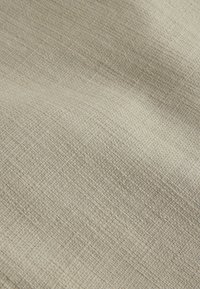 Light beige fabric with a textured weave, featuring a subtle pattern. The material appears soft and pliable, reflecting a natural finish.