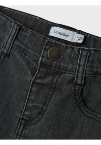 Svarta denimjeans med guldstickning, utrustade med en metallknapp, framfickor och en etikett som läser "Lil' Atelier."