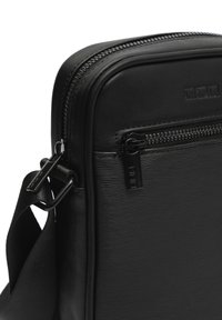 Čierna syntetická crossbody taška s textúrovaným povrchom, so zipsom a nastaviteľným popruhom. Má predné vrecko so zipsom.