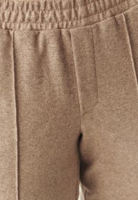 Brown, textured sweatpants with an elastic waistband, featuring side pockets and vertical seams for structure. Soft, fleece-like material.