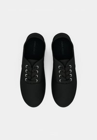 Et par sorte sorte svarte lissestoff-sko med svarte lisser og metalløyelet, sett ovenfra på en hvit bakgrunn.