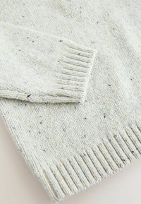 Maglione lavorato a maglia blu chiaro con macchie gialle e nere. Polsini e orlo a coste, texture morbida e trama leggermente larga.