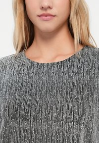 Detailní záběr dolní části obličeje a krku ženy, která má na sobě lesklý černý a stříbrný top s kulatým výstřihem.
