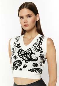 Top scurt fără mâneci, cu decolteu în V, din tricot alb, cu modele paisley negre contrastante. Textură moale și design ajustat, potrivit pentru stratificare.