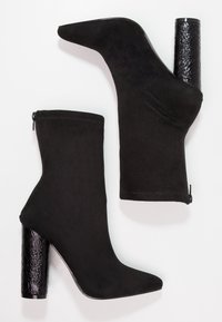 Botines negros de tobillo con textura de ante suave, punta afilada y tacón bloque texturizado negro brillante. Presentan un cierre de cremallera en el costado.