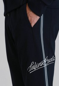 Marinefarbene Jogginghosen mit weißen Seitenstreifen, aus einem Baumwoll-Mischgewebe, mit einem modischen gestickten Logo nahe der Tasche für zusätzliche Details.