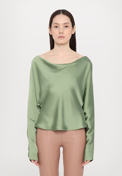 Haut en satin vert à manches longues avec un design décontracté, présentant une coupe ample et une texture lisse. Associé à un pantalon ajusté beige.