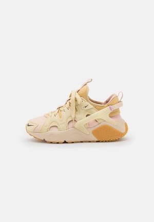Beige og lyserød sportssneaker med snørebånd, udskårne detaljer og tekstureret orange sål, set fra siden på en hvid baggrund.