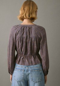 Lilla mønsterbluse med puffede ærmer, samlet talje og rund halsudskæring, parret med højtaljede blå denimjeans.