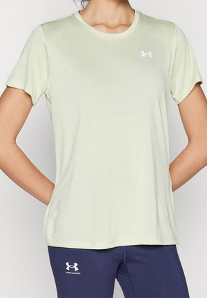 Personne portant un t-shirt à manches courtes Under Armour vert pâle et des leggings bleu marine avec le logo Under Armour, debout les mains derrière le dos.