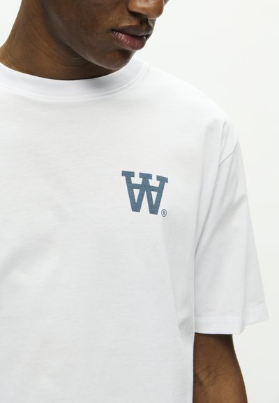 Weißes Baumwoll-T-Shirt mit einem blauen Grafikelement des Buchstabens "W" links auf der Brust. Kurze Ärmel und runder Halsausschnitt. Glatte Textur.