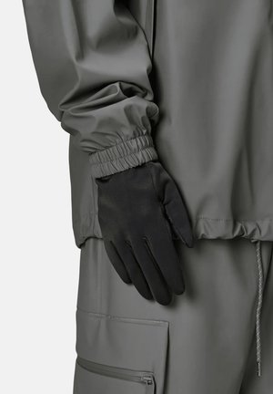 Veste imperméable grise avec poignets élastiques et poche cachée, associée à un gant noir avec une texture lisse et un design ajusté.