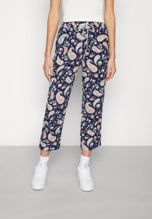 Osoba ubrana w granatowe krótkie spodnie z wielokolorowymi wzorami paisley, białe trampki, białe skarpetki i biały bezrękawnik.