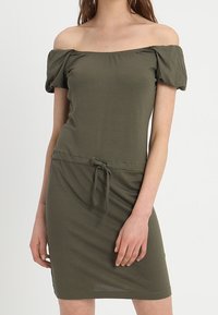 Robe olive verte à épaules dénudées avec des manches bouffantes, taille cintrée et détail à cordon. Fabriquée en tissu doux et texturé.